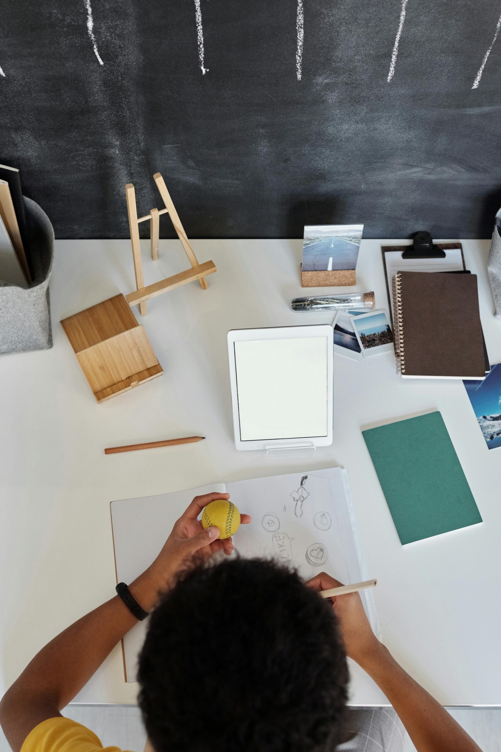 Overhead view of a teenager drawing at a desk with art supplies and tablet.